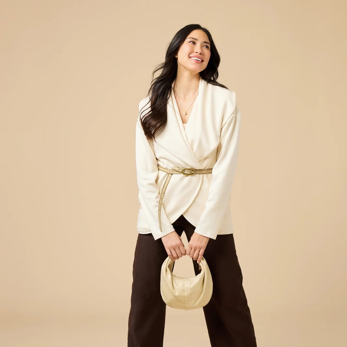 A woman wears an off-white SOFTIES - DREAMTECH EXAGGERATED COLLAR CARDIGAN with an exaggerated waterfall collar, cinched at the waist with a thin belt, and holds a matching handbag.