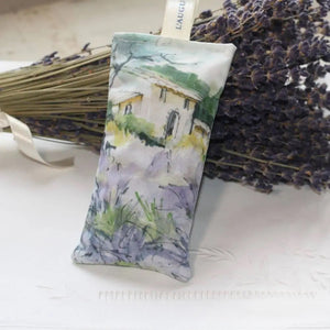 The L'AUGUSTE PROVENCE - FRENCH LAVENDER SACHET FROM PROVENCE features a painted house in a lavender field, stands upright with dried lavender in front, and is topped with a white "L'AUGUSTE" ribbon—authentic from Provence.
