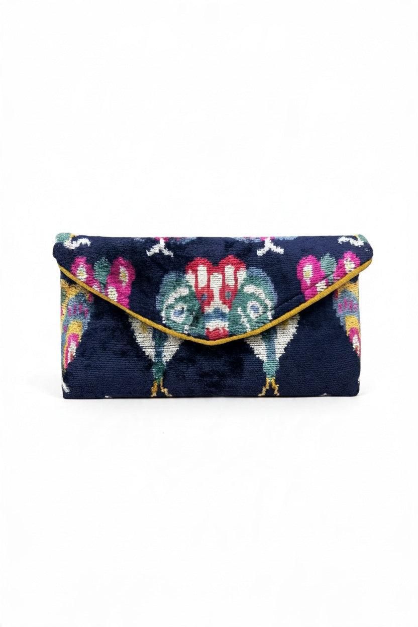 BALDIZ - LILY ENVELOPE CLUTCH IN OXFORD BLUE BUG handcrafted in dark blue velvet with a colorful bird pattern and gold-tone trim.