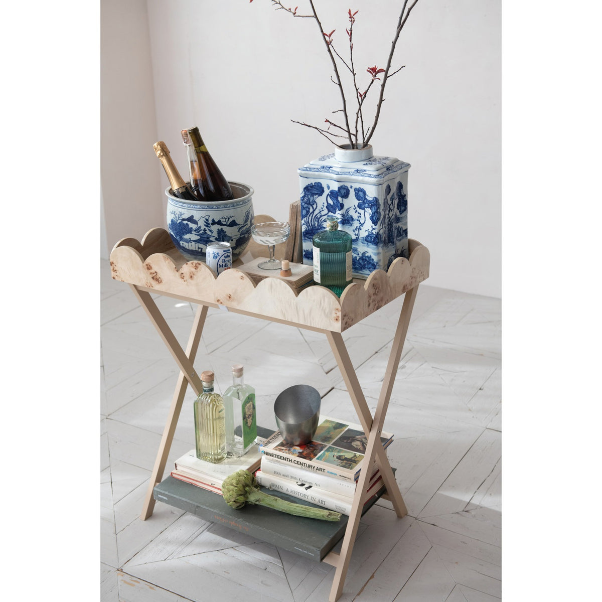 The CREATIVE COOP BURL WOOD VENEER FOLDING TABLE features crossed legs and a removable scalloped tray with a wavy rim and natural wood grain, blending charm with practical design.