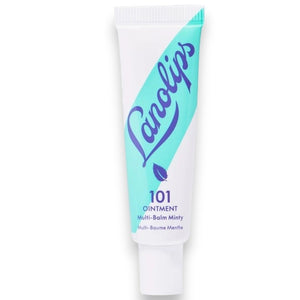 A woman holds a tube of LANOLIPS - 101 OINTMENT MULTI-BALM MINTY near her lips, dressed in a cream sweater against a blue background—highlighting LANOLIPS’ perfect minty hydration for dry lips.