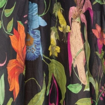 A close-up of the LAVI COUTURE - LIGEA FLORAL DRESS from LAVI highlights a vibrant botanical floral print with diverse flowers and green leaves on a black background. Bright oranges, pinks, blues, and greens add to the lively elegance of this exquisite Italian-made piece.