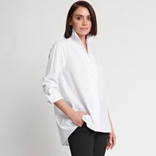 A person with short brown hair stands against a plain white background, wearing the HINSON WU - BETTY LONG SLEEVE TUNIC with the sleeves rolled up to the elbows and black pants. One hand is tucked into their pocket, and they look confidently at the camera.