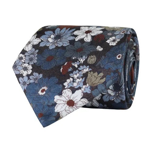 The AMANDA CHRISTENSEN - FLORAL SILK TWILL TIE IN SKY BLUE MELANGE features a sophisticated rolled floral pattern with blue, white, and brown flowers on a dark background, making it a refined addition to any collection of men’s accessories.