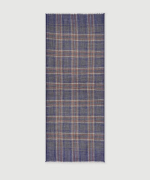 A man wearing a grey long-sleeve sweater and the HARTFORD - TARTAN WOOL SCARF IN INDIGO, GREY AND CAMEL stands against a white background, looking directly at the camera with his hands in his pockets—showcasing this classic men’s winter accessory from HARTFORD.
