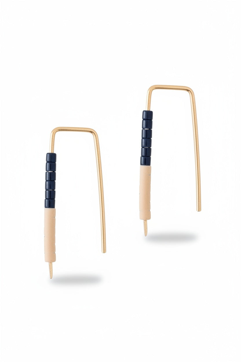 The ALICE RISE LITTLE QUILL EARRINGS IN NAVY AND CHALK are two small, L-shaped gold filled earrings with deep navy centers, shown parallel on a textured gray surface with their tips pointing downward.