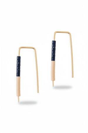 The ALICE RISE LITTLE QUILL EARRINGS IN NAVY AND CHALK are two small, L-shaped gold filled earrings with deep navy centers, shown parallel on a textured gray surface with their tips pointing downward.
