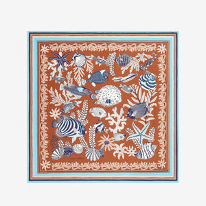 The INOUI EDITIONS - NEPTUNE SCARF IN GOLDEN BROWN by INOUI features detailed blue and white tropical fish, seaweed, shells, and coral on a brown background with an intricate blue, white, and brown border in cotton silk.