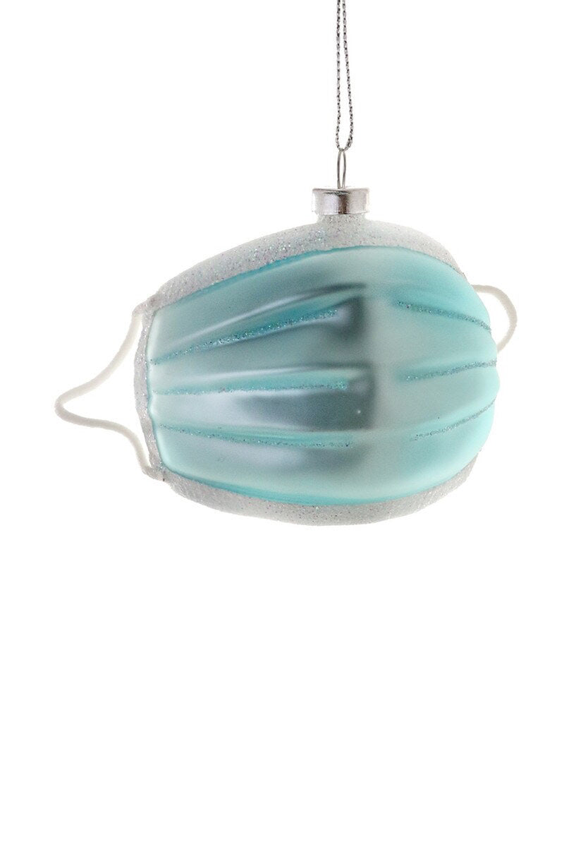 The MASK ORNAMENT by CODY FOSTER is a glass Christmas decoration styled as a light blue face mask, featuring glittery edges and a perfectly sized string for hanging.