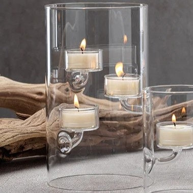 A SUSPENDED GLASS TEALIGHT HOLDER - LARGE by ZODAX holds several red-lit tealights, accented with pine branches and berries on a white surface, all set against a vibrant red background.