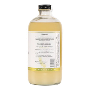 A clear glass bottle with a black cap containing Yes Cocktail Co.'s Ginger Citrus Cocktail Mixer is adorned with a white label featuring green accents. The text indicates it is crafted from fresh root, zesty lime, and has a spicy kick. The bottle holds 16 fl oz (473 ml).