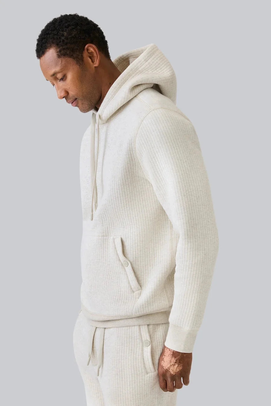 A man wearing a cream-colored, ribbed long-sleeve hooded sweatshirt and matching sweatpants.