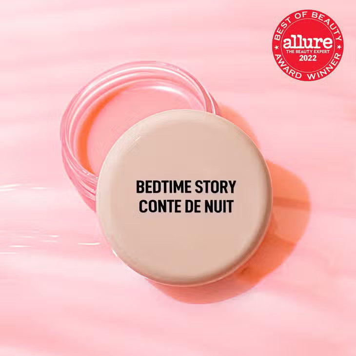 A round, beige container with the lid labeled &quot;JASON WU - GOODNIGHT MR WU LIP MASK&quot; from JASON WU BEAUTY is placed on a pink surface. The container is partially open, revealing a light pink overnight lip mask enriched with Shea Butter inside. An award badge in the top right corner reads &quot;Best of Beauty Allure 2022 Award Winner.