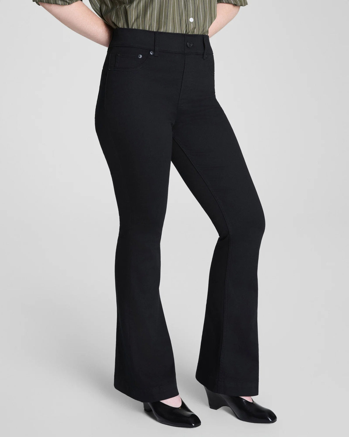 A person is shown from the back, wearing the SPANX - SPANXSHAPE EVERYWHERE PULL ON FLARE JEAN IN OBSIDIAN RINSE by SPANX with a green striped shirt, standing against a plain background to highlight the fit and style of the jeans.