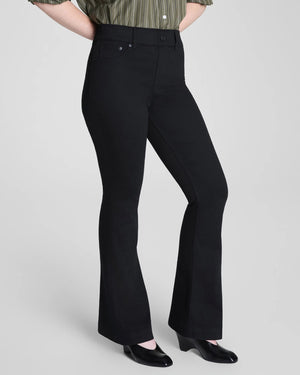 A person is shown from the back, wearing the SPANX - SPANXSHAPE EVERYWHERE PULL ON FLARE JEAN IN OBSIDIAN RINSE by SPANX with a green striped shirt, standing against a plain background to highlight the fit and style of the jeans.