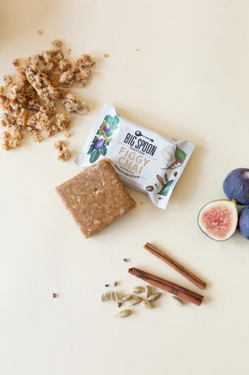The image displays the packaging of a &quot;BIG SPOON ROASTERS - FIGGY CHAI NUT BUTTER SNACK BAR.&quot; The white wrapper is adorned with illustrations of figs, spices, and nuts, emphasizing that it contains gluten-free whole grains and non-GMO pea protein. Additionally, it is free from dairy, gluten, soy, and palm oil, with a weight of 60g (2.1oz).