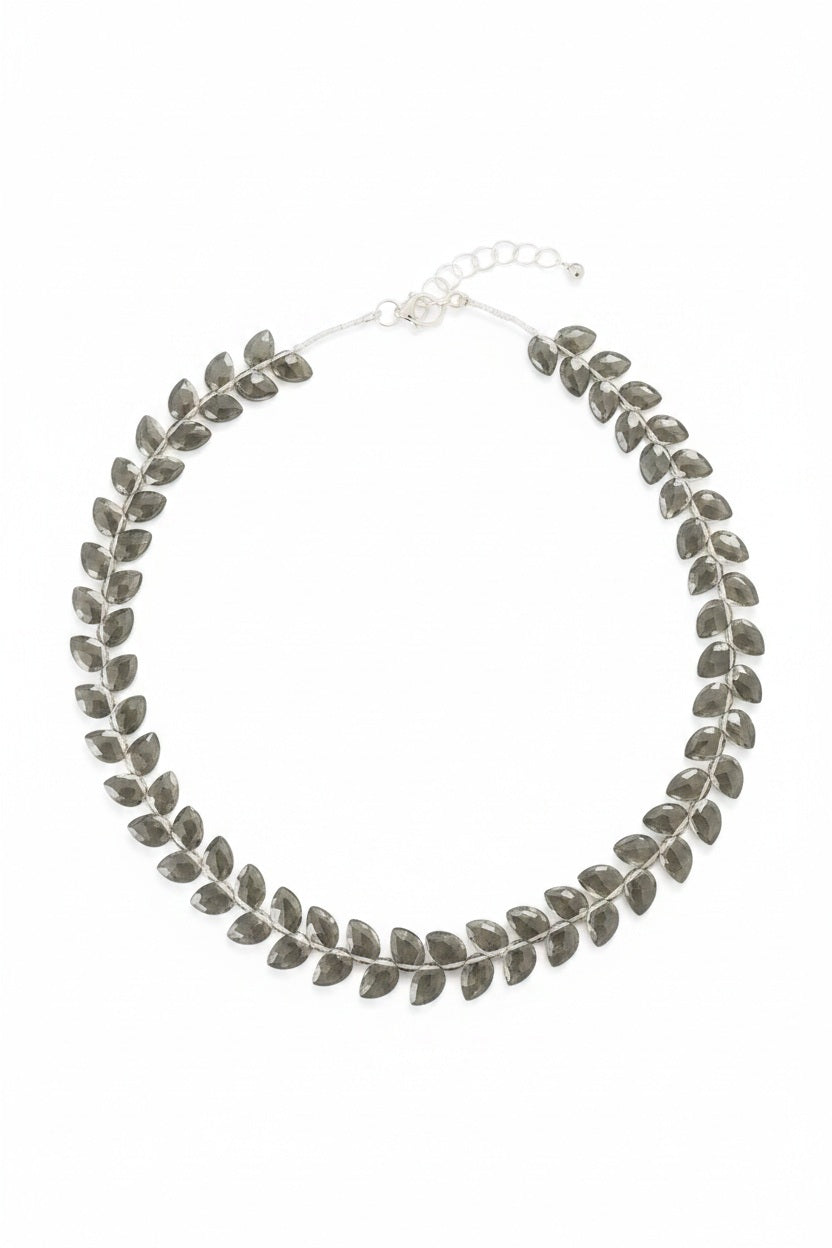 The ANN LIGHTFOOT Faceted Flat Herringbone Cut Smokey Quartz Necklace features leaf-shaped segments linked in a circular pattern, shown on a plain white background.