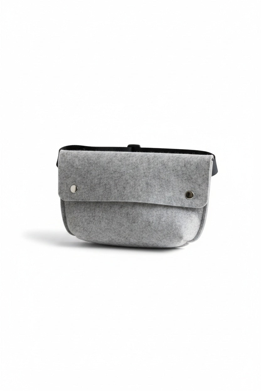 The WOOLBERRY - FELTED WOOL BELT BAG by WOOLBERRY is a small green belt bag crafted from felted wool, featuring a flap secured by two silver snap buttons, and is displayed against a white background.