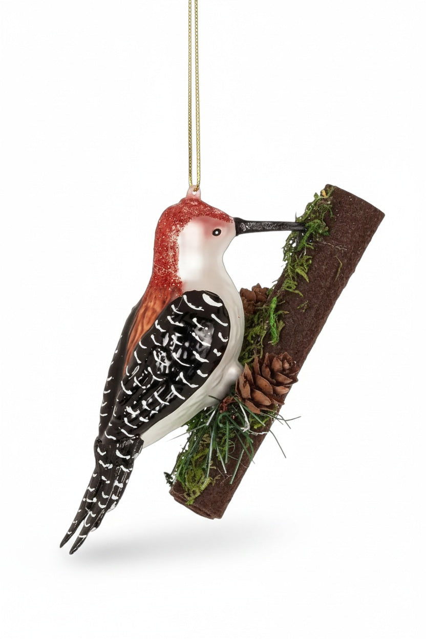 WOODPECKER ON TREE ORNAMENT featuring a glass woodpecker perched on a decorative branch with small pinecones and moss, perfect for woodland holiday decor.