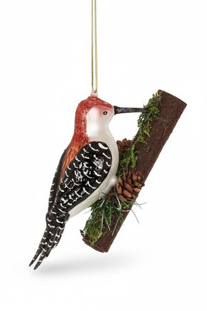 WOODPECKER ON TREE ORNAMENT featuring a glass woodpecker perched on a decorative branch with small pinecones and moss, perfect for woodland holiday decor.