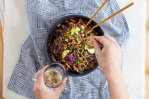 A jar of JACOBSEN SALT CO. INFUSED BLACK GARLIC SALT, featuring a black label and white lid, rests on a light beige surface against a plain light gray background.
