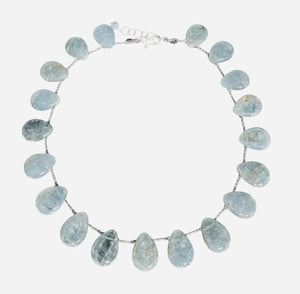 A mannequin in a textured, cream faux fur vest showcases the ANN LIGHTFOOT - BRAIDED RAS DU COU FAN CALCITE NECKLACE, featuring blue calcite stones on gold-tone links with a sterling silver clasp, against a softly lit background.