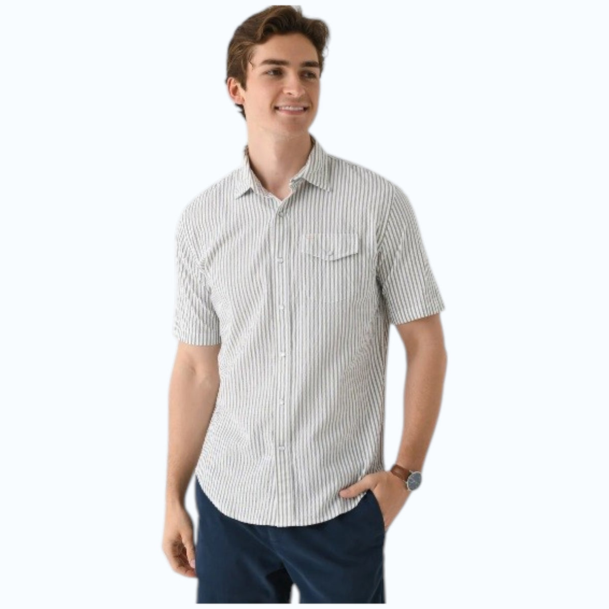 A young man, smiling with one hand in his pocket, wears CRIQUET’s Short Sleeve Performance Seersucker Pearl Snap Shirt in Sage and navy blue pants.