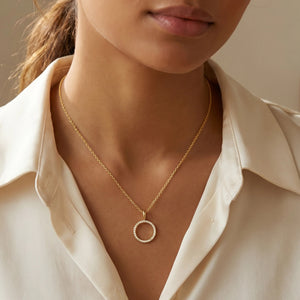 The ELLA STEIN - STANDING O PENDANT NECKLACE by ELLA STEIN features a delicate gold link chain showcasing a circular gold-plated pendant, elegantly outlined with small white gemstones. Photographed on a plain white background, this simple yet sophisticated necklace brings together the enduring appeal of stainless steel jewelry and modern design.