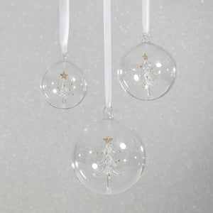 The ZODAX CLEAR GLASS BALL ORNAMENT WITH TREE INSIDE is a 4-inch ornament featuring a white glass Christmas tree topped with a gold star, suspended by a beige ribbon, beautifully displayed against a white background.