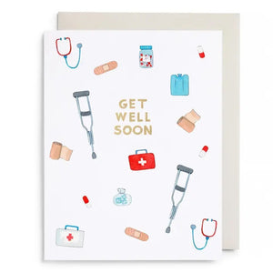 The E. FRANCES - FIRST AID KIT CARD from E. FRANCES PAPER is a watercolor greeting card featuring "Get Well Soon" in gold letters, surrounded by illustrations of crutches, stethoscopes, bandages, pills, first aid kits, pill bottles, and an ice pack on a white background—thoughtfully designed as a sympathy card and proudly made in the USA.