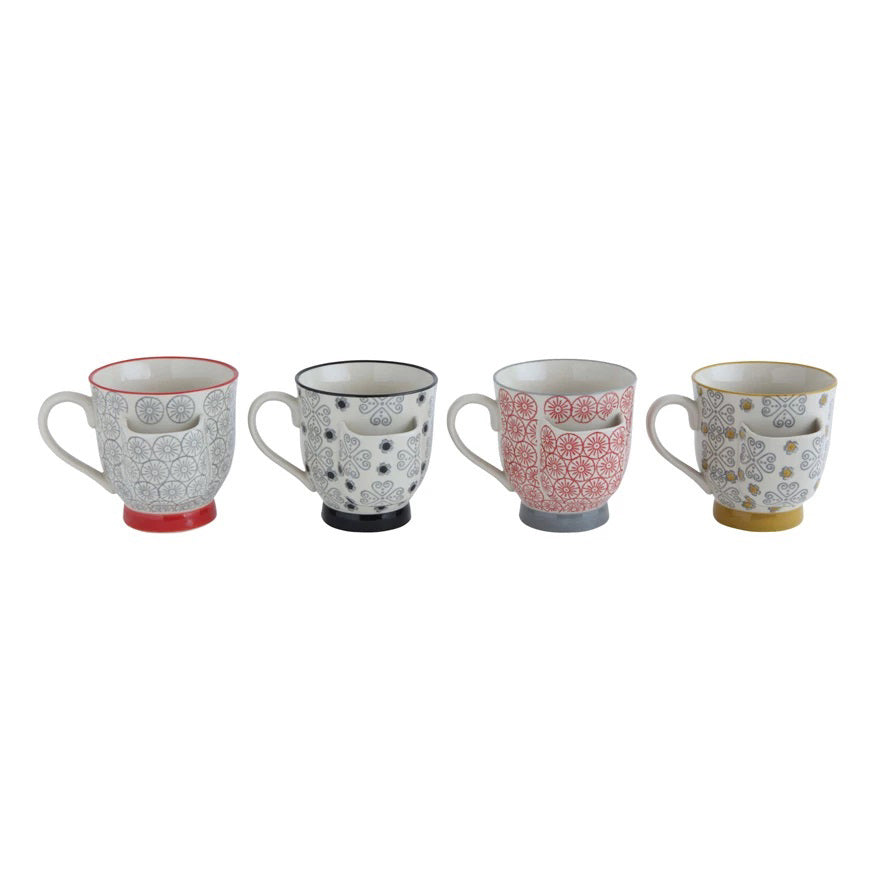 Four intricately patterned stoneware mugs from Creative Coop, each with a unique color, are lined up on a wooden plank against a plain background. Their unique designs create a visually appealing arrangement and, as the &quot;Mug with Tea Bag Holder,&quot; they are microwave safe for practicality.