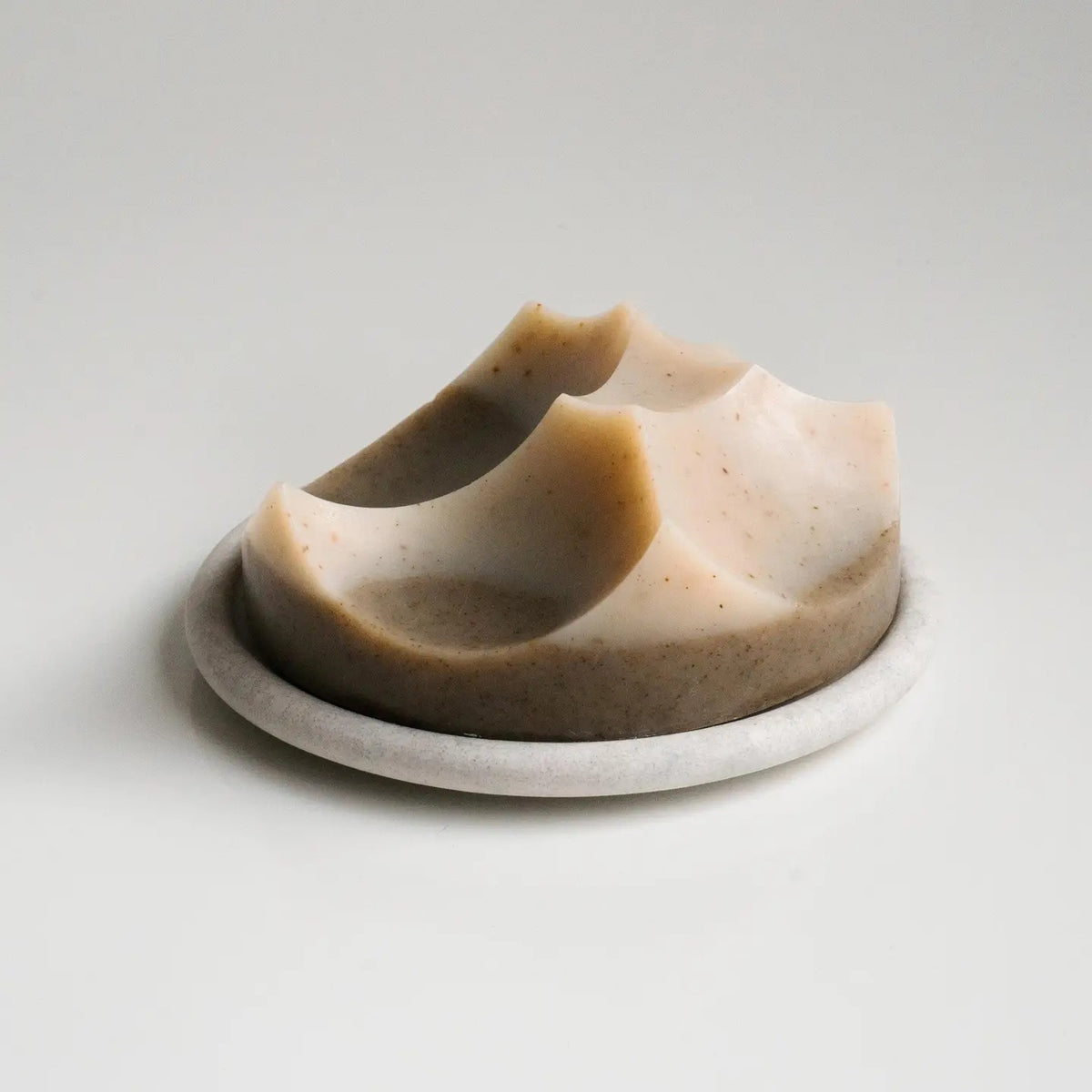 The UME - GREY BOUTON ERODE SOAP DISH by UME STUDIO features a large, round, light gray design inspired by the Bouton series, echoing the look of a minimalist handmade tray or concrete dish.