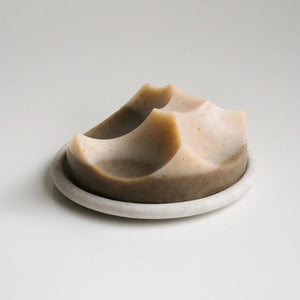 The UME - GREY BOUTON ERODE SOAP DISH by UME STUDIO features a large, round, light gray design inspired by the Bouton series, echoing the look of a minimalist handmade tray or concrete dish.