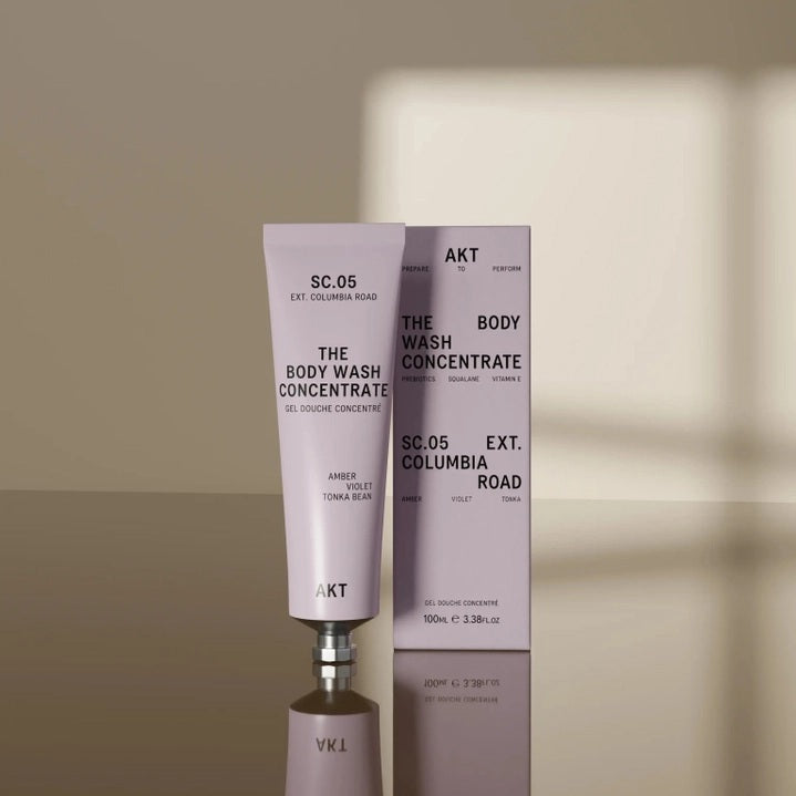 A tube of AKT LONDON BODY WASH CONCENTRATE COLUMBIA ROAD—a luxurious concentrated body wash enriched with olive squalane—stands upright in front of its matching box on a neutral surface, with a soft shadow in the background.