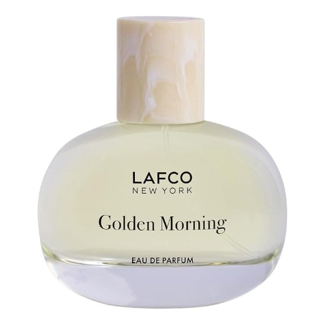 A transparent perfume bottle labeled “LAFCO - FINE FRAGRANCE, GOLDEN MORNING 50ML” by LAFCO features a round, marble-textured cream cap and is displayed against a plain white background. This floral scent is crafted as a vegan and cruelty-free fine fragrance, designed to deliver a sophisticated and conscious olfactory experience.