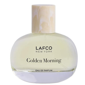 A transparent perfume bottle labeled “LAFCO - FINE FRAGRANCE, GOLDEN MORNING 50ML” by LAFCO features a round, marble-textured cream cap and is displayed against a plain white background. This floral scent is crafted as a vegan and cruelty-free fine fragrance, designed to deliver a sophisticated and conscious olfactory experience.