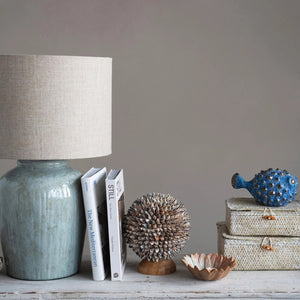The CREATIVE COOP AQUA STONEWARE LAMP WITH LINEN SHADE features a nature-inspired design with a muted green textured ceramic base and a beige linen shade, set against a white background.