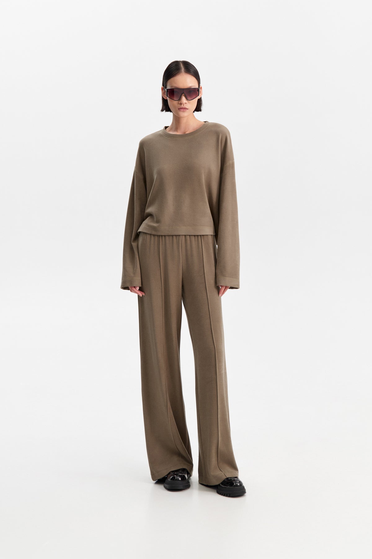 The ELEH - THE SCALA SWEATSHIRT by ELEH is a taupe, long-sleeve cropped sweatshirt featuring dropped shoulders and a relaxed fit, shown against a plain white background.