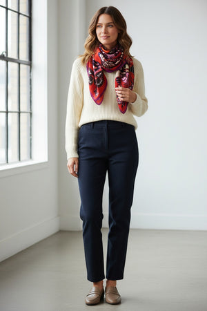 A person with straight dark hair wears a cream sweater and the INOUI EDITIONS - PAPILLONS (BUTTERFLIES) Square Wool Scarf in Red by INOUI, featuring butterfly wing patterns, while standing against a plain white background.