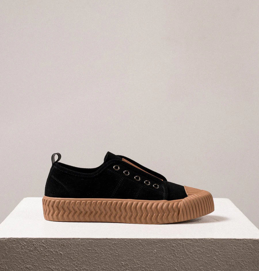 Introducing the DANIELLA LEHAVI - OSAKA SNEAKER by DANIELLA LEHAVI: Black sneakers featuring brown rubber soles and decorative brown straps across the top. They highlight a contemporary design with circular metal eyelets on the sides and are presented on a white platform against a simple, light-colored background.