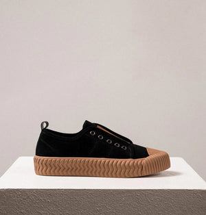 Introducing the DANIELLA LEHAVI - OSAKA SNEAKER by DANIELLA LEHAVI: Black sneakers featuring brown rubber soles and decorative brown straps across the top. They highlight a contemporary design with circular metal eyelets on the sides and are presented on a white platform against a simple, light-colored background.