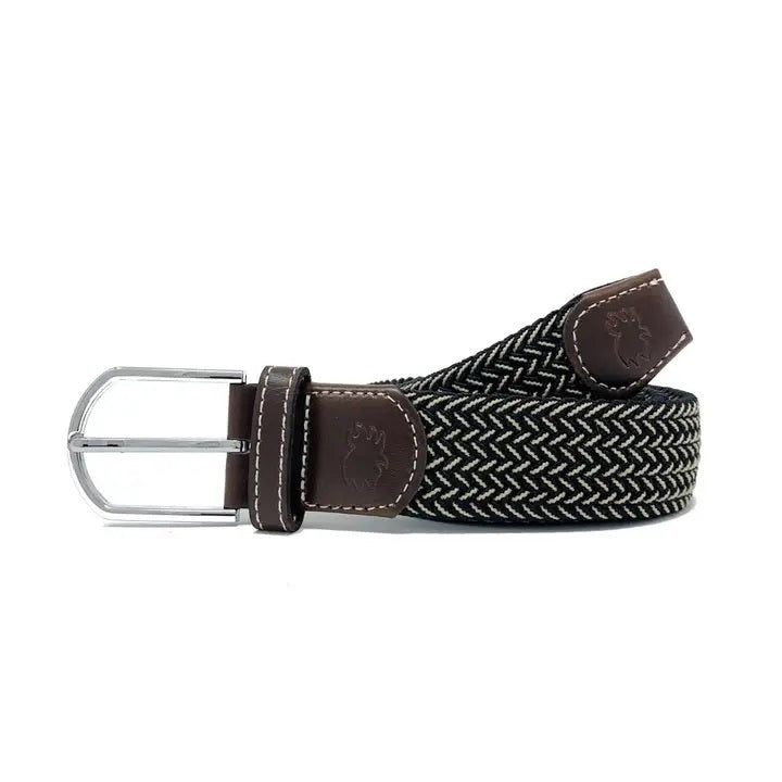 The ROOSTAS - MAUI WOVEN STRETCH BELT by ROOSTAS features a black and white zigzag pattern, brown leather ends, a silver buckle, and an adjustable clasp for the perfect fit.