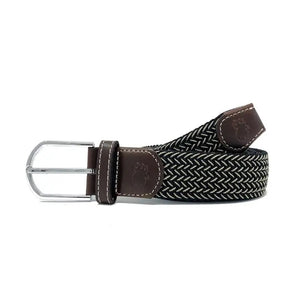 The ROOSTAS - MAUI WOVEN STRETCH BELT by ROOSTAS features a black and white zigzag pattern, brown leather ends, a silver buckle, and an adjustable clasp for the perfect fit.