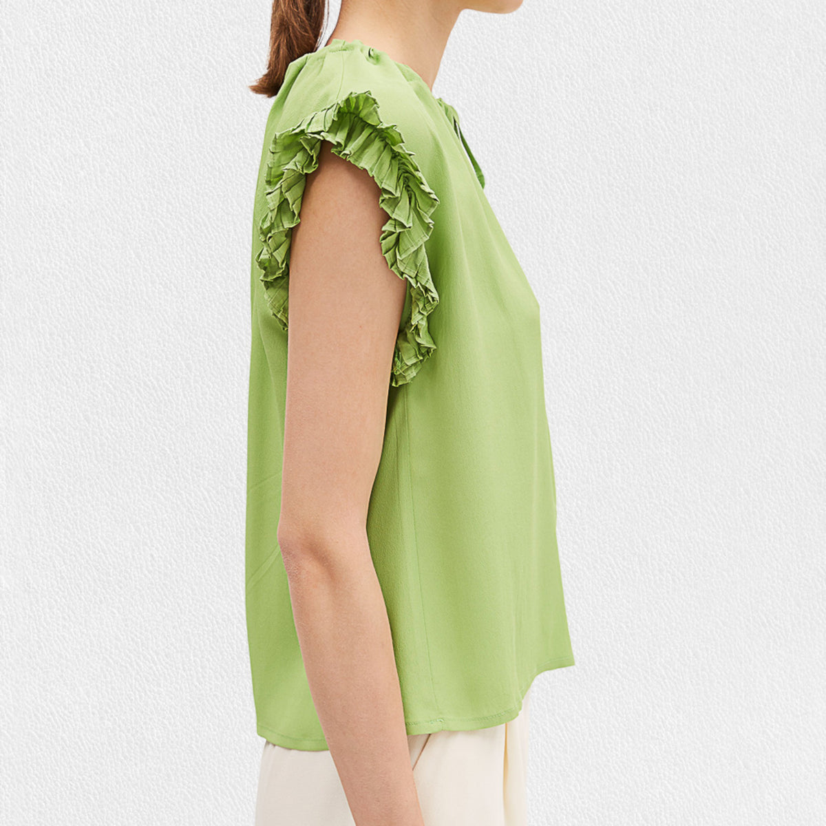 A woman wears the MEIMEIJ Cap Sleeve Blouse, a light green viscose top with ruffle cap sleeves and a tied neckline from MEIMEIJ, paired with white bottoms against a plain light background.