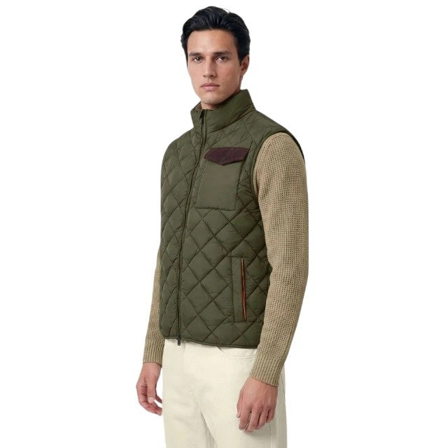 A person stands facing forward, wearing the SAVE THE DUCK - FABRICE Puffer Vest in Snake Green with Plumtech® padding over a beige sweater, paired with white pants and tan shoes, against a plain light background.