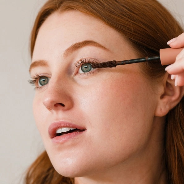 Three close-up shots of a blue eye: lashes with no mascara (before), lashes enhanced with MINORI - MOTHER OF LASHES MASCARA, BROWN by MINORI, and lashes with black mascara, highlighting the color and definition differences.