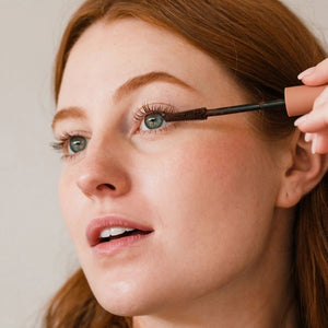Three close-up shots of a blue eye: lashes with no mascara (before), lashes enhanced with MINORI - MOTHER OF LASHES MASCARA, BROWN by MINORI, and lashes with black mascara, highlighting the color and definition differences.
