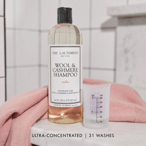 A 16 fl oz (473 ml) bottle of THE LAUNDRESS - WOOL AND CASHMERE SHAMPOO 16OZ, featuring a cedar scent. The clear bottle is topped with a black cap and has a white label with black text specifying the brand, THE LAUNDRESS, and product type. This gentle wash detergent, formulated with bio-based ingredients, is ideal for wool, cashmere, and knit blends.