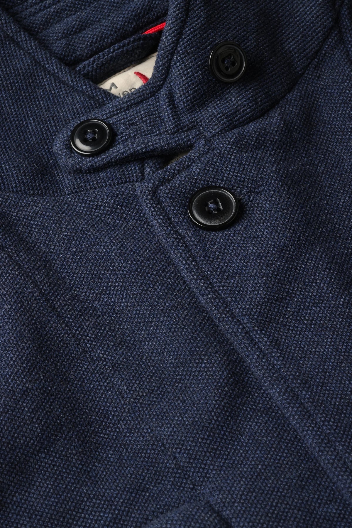 A person wearing the RELWEN - PIQUE TRAP BLAZER IN NAVY HEATHER over a checked shirt and green cargo pants stands with hands in pockets against a plain background, showcasing the blazer’s relaxed fit.