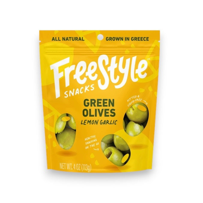A yellow packet of FREESTYLE - LEMON GARLIC GREEN OLIVES from FREESTYLE SNACKS, featuring green olives flavored with extra virgin olive oil. The packaging highlights the "all-natural" ingredients and notes that the olives are "grown in Greece." Weighing 4 oz (113g), the pack showcases images of green olives alongside phrases such as "pitted &amp; unpasteurized" and "healthy snacking on the go.